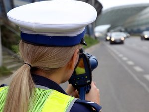 policjantka mierzy prędkość miernikiem prędkości, w tle droga
