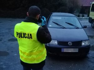 mężczyzna w kamizelce odblaskowej z napisem POLICJA trzyma aparat i fotografuje samochód