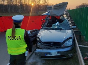 policjantka w kamizelce  odblaskowej stoi przed rozbitym w wypadku samochodem