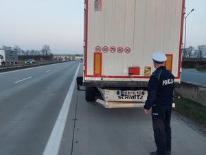 policjant stoi za samochodem ciężarowym na autostradzie, w tle przejeżdżające samochody