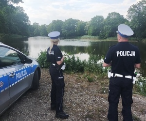 policjanci stoją obok radiowozu, w tle zbiornik wodny