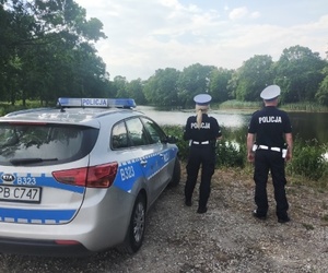 policjanci stoją obok radiowozu, w tle zbiornik wodny