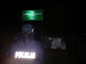 noc, policjantka stoi przy tablicy z napisem Rodzinny Ogród Działkowy