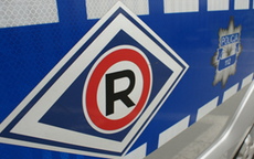 symbol ruchu drogowego w postaci litery R na białym tle w czerwonym okręgu na tle niebieskiego rombu na drzwiach radiowozu