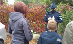 kobieta i dziecko odwróceni plecami, w tle policjant