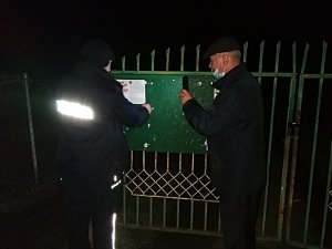 policjant przyczepia do tablicy ogłoszeń kartkę z danymi dzielnicowych, obok stoi mężczyzna
