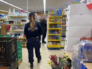 zdjęcie przedstawia policjantkę w sklepie podczas kontroli z pracownikami Sanepidu, obok półki wypełnione towarem