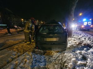 zdjęcie przedstawia rozbity samochód przy drzewie w tle widać światła karetki pogotowia