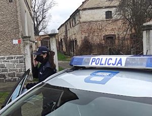 zdjęcie przedstawia policjantkę przy radiowozie, która trzyma przy uchu telefon