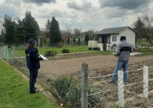 policjantka stoi przy ogrodzeniu ogródka działkowego, obok mężczyzna