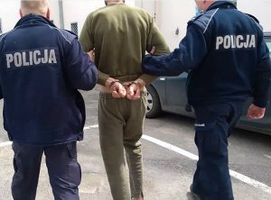 dwóch policjantów prowadzi zatrzymanego mężczyznę z kajdankami na rękach