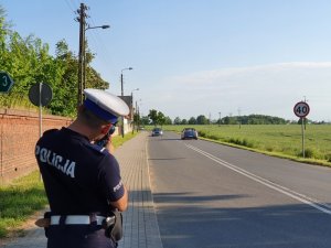 policjant stoi przy drodze, w dłoniach trzyma miernik prędkości , w tle droga