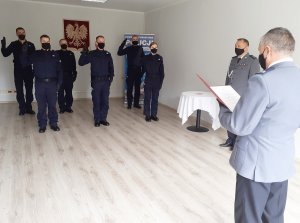 Komendant Powiatowy Policji odczytuje treść roty ślubowania, w tle stoją policjanci z uniesioną ręką