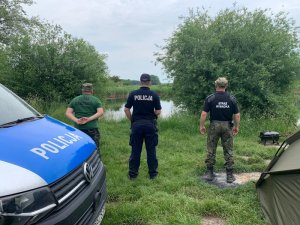 funkcjonariusze straży rybackiej oraz policjant stoją nad brzegiem rzeki