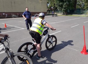 chłopiec w kamizelce odblaskowej siedzi na rowerze, w tle widać policjanta