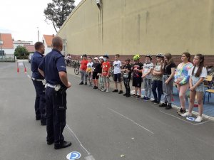 dzieci stoją w rzędzie na boisku, przed nimi stoi dwóch policjantów