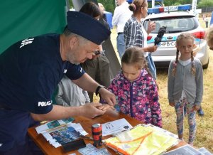 policjant stoi przy stoliku i wykonuje odciski palców dziewczynki, na stoliku ulotki, elementy odblaskowe