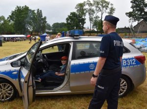 dziecko siedzi w radiowozie, obok stoi policjant